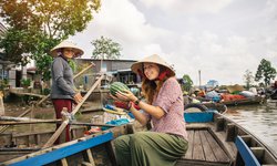 Touristin während einer Rundreise auf einem Floating Market. Thailänderin verkauft Ihr frische Früchte von Boot zu Boot.