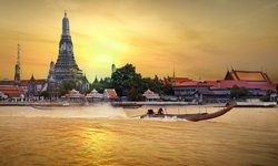 Tempel Wat Arun in Bangkok, ein Pflichtbesuch auf jeder Thailand Rundreise. Im Vordergrund Boote auf dem Fluss, am Horizont geht die Sonne über Thailands Hauptstadt unter